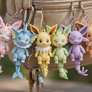 May include: A collection of six articulated character keychains featuring pastel-colored creatures with large ears and tails. The figures include pink, blue, yellow, light green, purple, and tan designs, each attached to a silver metal keyring.