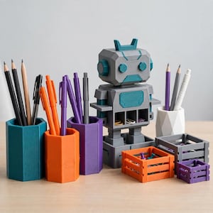 May include: A desk organiser set featuring a grey robot figure with teal accents, three hexagonal pencil holders in teal, orange, and purple, a white geometric cup, and three small rectangular crates in orange, grey, and purple for supplies.