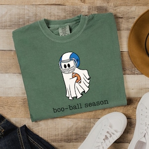 May include: A green t-shirt with a ghost wearing a football helmet and holding a football. The text "boo-ball season" is printed below the ghost.