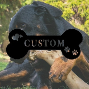 Könnte beinhalten: Schwarzer Metall-Hunde-Knochen mit dem Wort "CUSTOM" und Pfotenabdrücken. Ein schwarz-brauner Hund kaut auf einem Knochen.