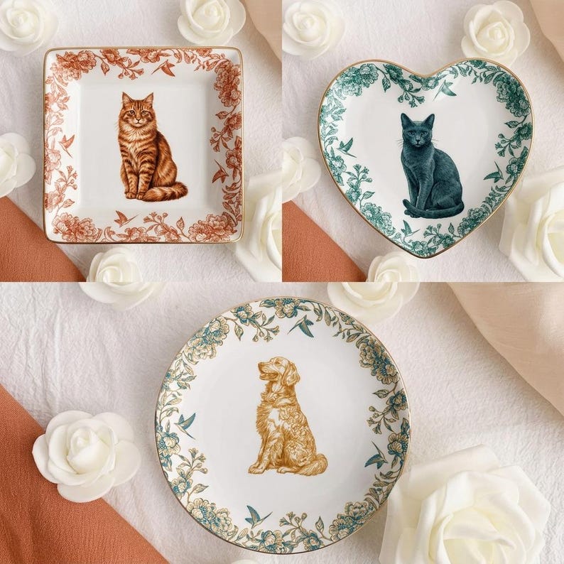 Puede incluir: Tres platos decorativos de cer&aacute;mica con ilustraciones de animales. Un plato cuadrado presenta un gato atigrado marr&oacute;n, un plato en forma de coraz&oacute;n tiene un gato gris y un plato redondo muestra un golden retriever. Cada plato tiene un borde floral.