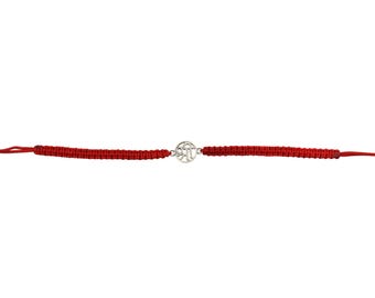 May include: A red woven bracelet with a silver-colored charm. The charm has a circular design with intricate details. The bracelet is made of a thick, woven red cord. The bracelet is displayed against a white background.