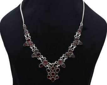 Puede incluir: Un collar de plata con un colgante que presenta un grupo de piedras preciosas rojas. El collar tiene una cadena delicada y está adornado con múltiples piedras rojas de varias formas.