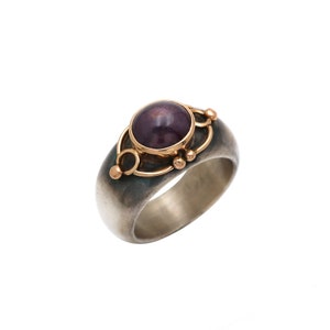 May include: A silver ring with a dark purple gemstone set in a gold bezel. The ring has a textured band and gold accents.