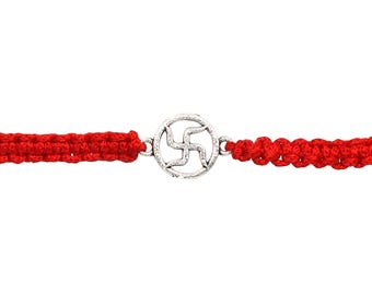May include: A red macrame bracelet featuring a silver-colored charm with a swastika design. The bracelet is made of a thick, woven red cord. The charm is circular and has a detailed, openwork pattern.