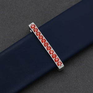 May include: A silver watch band buckle with a row of red gemstones.