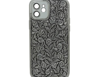 Puede incluir: Funda de teléfono plateada con un intrincado diseño floral. La funda tiene un acabado metálico y un diseño en relieve detallado de flores y hojas. El área de la cámara es plateada y la funda tiene un borde liso y redondeado.