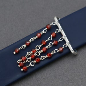 May include: A silver watch band buckle with a dangling charm of red beads and silver chains.
