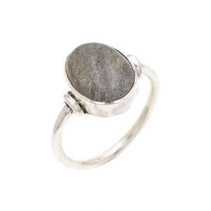 May include: A silver ring with a grey oval-shaped gemstone. The ring has a simple design with a wire wrapped around the stone.