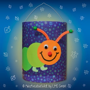 Könnte beinhalten: Eine lilafarbene Papierlaterne mit einem grünen und orangenen Raupenmotiv. Die Raupe hat Kulleraugen und einen lächelnden Mund. Die Laterne hat eine weiße Schnur zum Aufhängen.