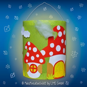 May include: A green paper lantern with a mushroom design. The lantern has a white handle and is decorated with red and white polka dots. The text "Kiki's kreativeWelt by LMS GmbH" is printed on the bottom of the lantern.