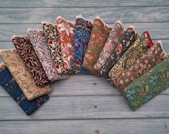 May include: A collection of twelve rectangular fabric pouches arranged in a fan shape. Each pouch features a distinct floral or botanical print in various colours including blue, green, red, and brown. Each pouch has a small wooden button closure.