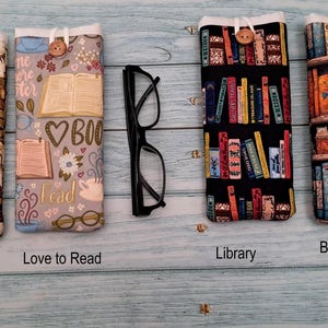 Puede incluir: Cuatro estuches rectangulares de tela para gafas con cierre de bot&oacute;n, con estampados de libros antiguos, libros abiertos con el texto Love to Read, estanter&iacute;as de biblioteca y libros en estantes, junto a unas gafas negras.