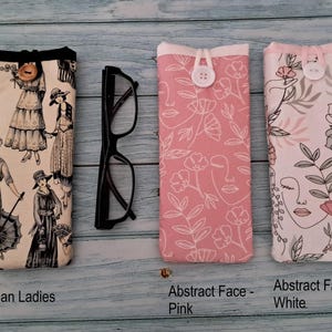 Puede incluir: Tres estuches rectangulares de tela para gafas con cierre de bot&oacute;n y un par de gafas negras. El primer estuche muestra Victorian Ladies, el segundo es Abstract Face - Pink y el tercero es Abstract Face - White con dibujos lineales florales.