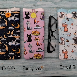 Puede incluir: Tres fundas de tela para gafas con cierre de bot&oacute;n. La primera es azul oscuro con lunas amarillas y gatos durmiendo. La segunda es morado claro con varios gatos. La tercera es azul claro con gatos y mariposas.