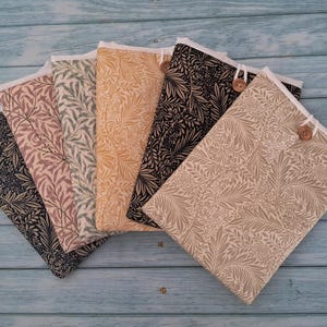 May include: A collection of five rectangular fabric sleeves arranged in a fan shape. Each sleeve features a detailed botanical leaf pattern in various colours including black, dusty pink, sage green, mustard yellow, and beige, with a wooden button closure.
