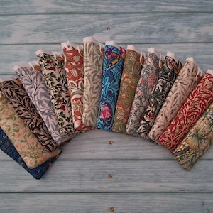 May include: A collection of fabric cases, each with a unique floral or botanical pattern in various colors. The cases are arranged in a semi-circle, showcasing a variety of designs and textures. Each case has a white top and a button closure.