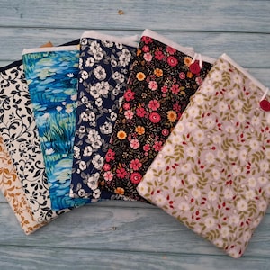 May include: A collection of six rectangular fabric pouches arranged in a fan shape. Each pouch features a distinct pattern, including gold floral, black and white scrollwork, blue water lilies, navy floral, black floral, and a light floral print.