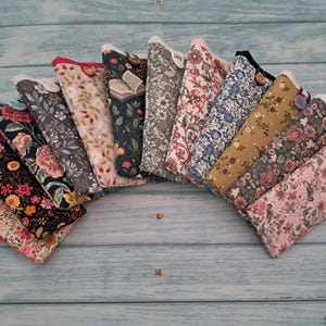 May include: A selection of fabric glasses cases, each featuring a different floral design. The cases are displayed in a semi-circular arrangement, with colours such as pink, black, blue, and green. Some cases have button fastenings.