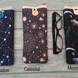 Puede incluir: Tres fundas de tela para gafas con cierre de bot&oacute;n. La primera, etiquetada Constellation, es azul marino con estrellas blancas. La segunda, Celestial, es negra con motivos de sol y luna. La tercera, Moon Garden, es negra con polillas y lunas crecientes.