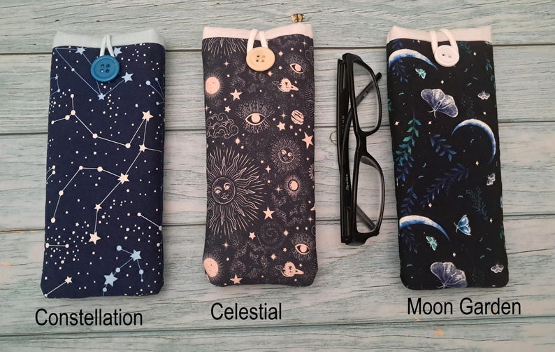 Puede incluir: Tres fundas de tela para gafas con cierre de bot&oacute;n. La primera, etiquetada Constellation, es azul marino con estrellas blancas. La segunda, Celestial, es negra con motivos de sol y luna. La tercera, Moon Garden, es negra con polillas y lunas crecientes.