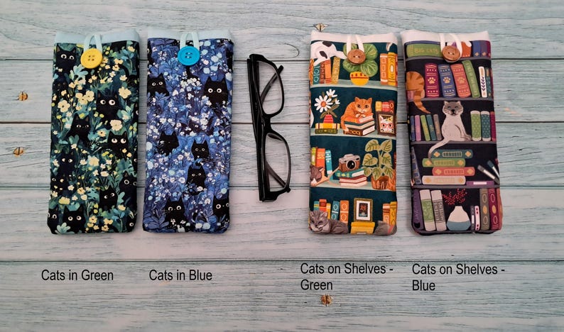 Puede incluir: Cuatro estuches rectangulares de tela con cierres de bot&oacute;n y un par de gafas negras. Dos estuches presentan patrones de gatos negros sobre fondos verde y azul. Dos estuches presentan patrones de gatos y estanter&iacute;as de libros.