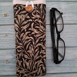 May include: A black and beige floral print glasses case with a wooden button closure. Next to the case are black framed eyeglasses.