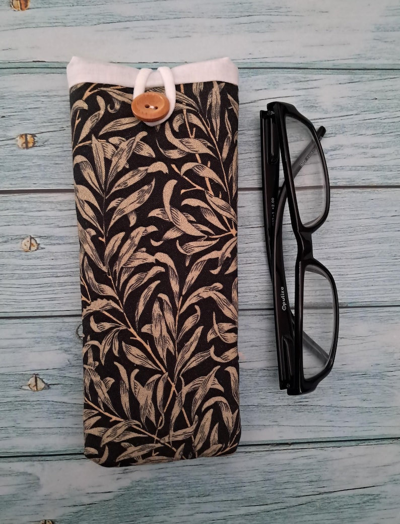May include: A black and beige floral print glasses case with a wooden button closure. Next to the case are black framed eyeglasses.
