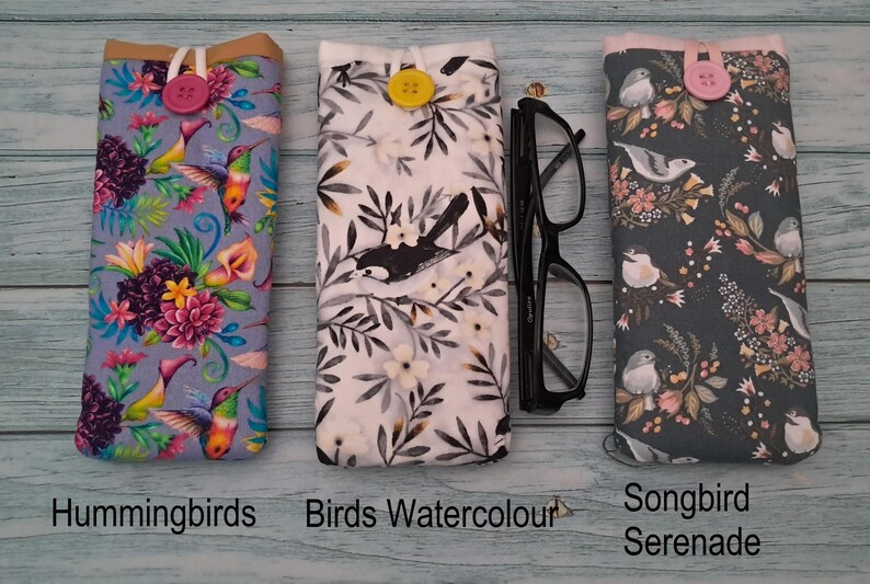 Puede incluir: Tres fundas de tela para gafas con cierre de bot&oacute;n. La funda de la izquierda presenta colibr&iacute;es y flores, la central tiene un patr&oacute;n de aves en blanco y negro con un bot&oacute;n amarillo, y la derecha muestra p&aacute;jaros cantores y motivos florales.