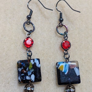 May include: A pair of dangle earrings with black metal hooks, red glass beads, and square black and white glass tiles. The tiles have a speckled pattern.