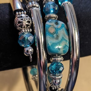 May include: A set of three silver bangle bracelets with turquoise blue beads and a larger turquoise blue agate stone charm.