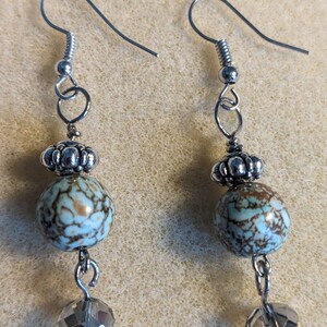 May include: A pair of silver dangle earrings with a light blue and brown patterned bead and a clear crystal bead on each earring.