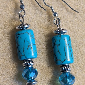 May include: A pair of turquoise and silver dangle earrings. The earrings feature a turquoise bead with silver accents and a crystal bead.