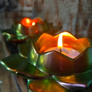 May include: Two iridescent green lotus-shaped candle holders with a teal green glaze. The candle holders are lit with tea lights, creating a warm glow.