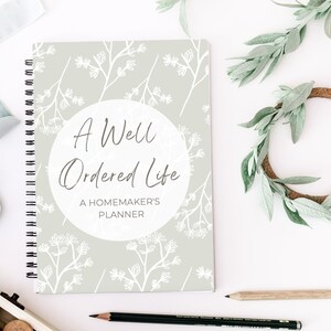 May include: A green and white spiral bound planner with the title "A Well Ordered Life: A Homemaker's Planner". The cover features a white floral pattern on a light green background.