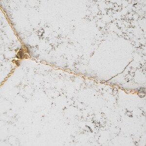 May include: A gold chain necklace with a lobster clasp and a small clear crystal at the end.