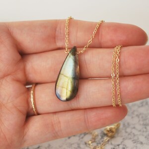 May include: A gold chain necklace with a teardrop-shaped labradorite pendant. The pendant has a green, gold, and black iridescent sheen.