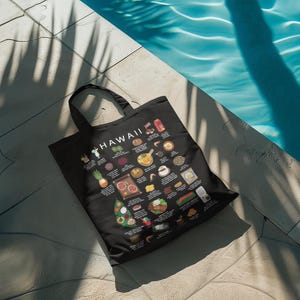 May include: Black tote bag featuring a colorful illustration of Hawaiian cuisine. The bag displays various dishes and the word "HAWAII" in white. The bag is made of a durable material and has black handles.