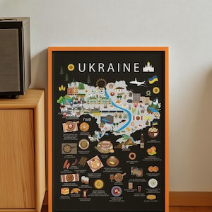 Puede incluir: Un póster enmarcado con borde naranja muestra un mapa de Ucrania con ilustraciones de comida y lugares emblemáticos. La palabra "UKRAINE" está en la parte superior. El póster está sobre un mueble de madera.