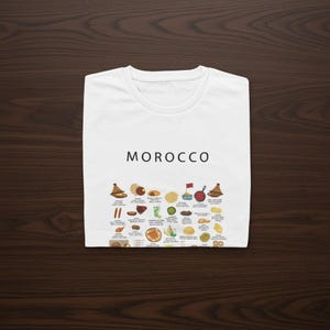 T-shirt featuring a colorful illustration of traditional Moroccan foods, including a steaming tagine, fluffy couscous, bowl of harira soup, fresh mint tea, and assorted sweet pastries, styled in a vibrant street-food design