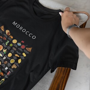 T-shirt featuring a colorful illustration of traditional Moroccan foods, including a steaming tagine, fluffy couscous, bowl of harira soup, fresh mint tea, and assorted sweet pastries, styled in a vibrant street-food design