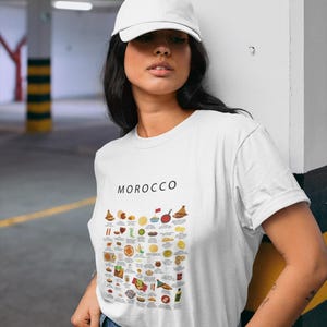 T-shirt featuring a colorful illustration of traditional Moroccan foods, including a steaming tagine, fluffy couscous, bowl of harira soup, fresh mint tea, and assorted sweet pastries, styled in a vibrant street-food design
