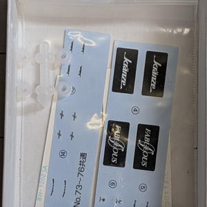 Pode incluir: Uma caixa branca contendo pe&ccedil;as de um kit de modelo. Inclui pe&ccedil;as de pl&aacute;stico transparente, decalques azuis com as palavras "FABULOUS" e "kr&auml;nze" e texto japon&ecirc;s. O kit parece ser para um carro ou ve&iacute;culo modelo.