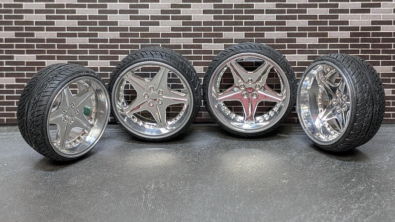 Pode incluir: Quatro rodas cromadas para carro com pneus pretos. As rodas t&ecirc;m um design em forma de estrela de cinco pontas. Os pneus t&ecirc;m um padr&atilde;o texturizado e ranhurado. As rodas s&atilde;o exibidas contra uma parede de tijolos.