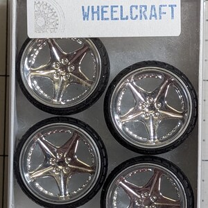 Pode incluir: Quatro rodas de carro em miniatura com acabamento cromado e pneus pretos, apresentadas numa embalagem de pl&aacute;stico transparente. As rodas t&ecirc;m um design de cinco raios e est&atilde;o rotuladas como "WHEELCRAFT" numa etiqueta branca.