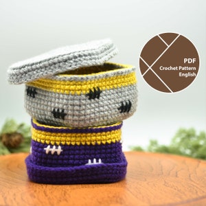 May include: Three crocheted storage baskets with lids. The top basket is gray with black accents, the middle basket is purple with white accents, and the bottom basket is yellow with white accents. PDF Crochet Pattern English.