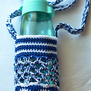 May include: A clear water bottle with a teal lid is encased in a handmade crochet holder. The holder is navy blue and white, with a matching strap. The crochet design features a mix of solid and openwork patterns.