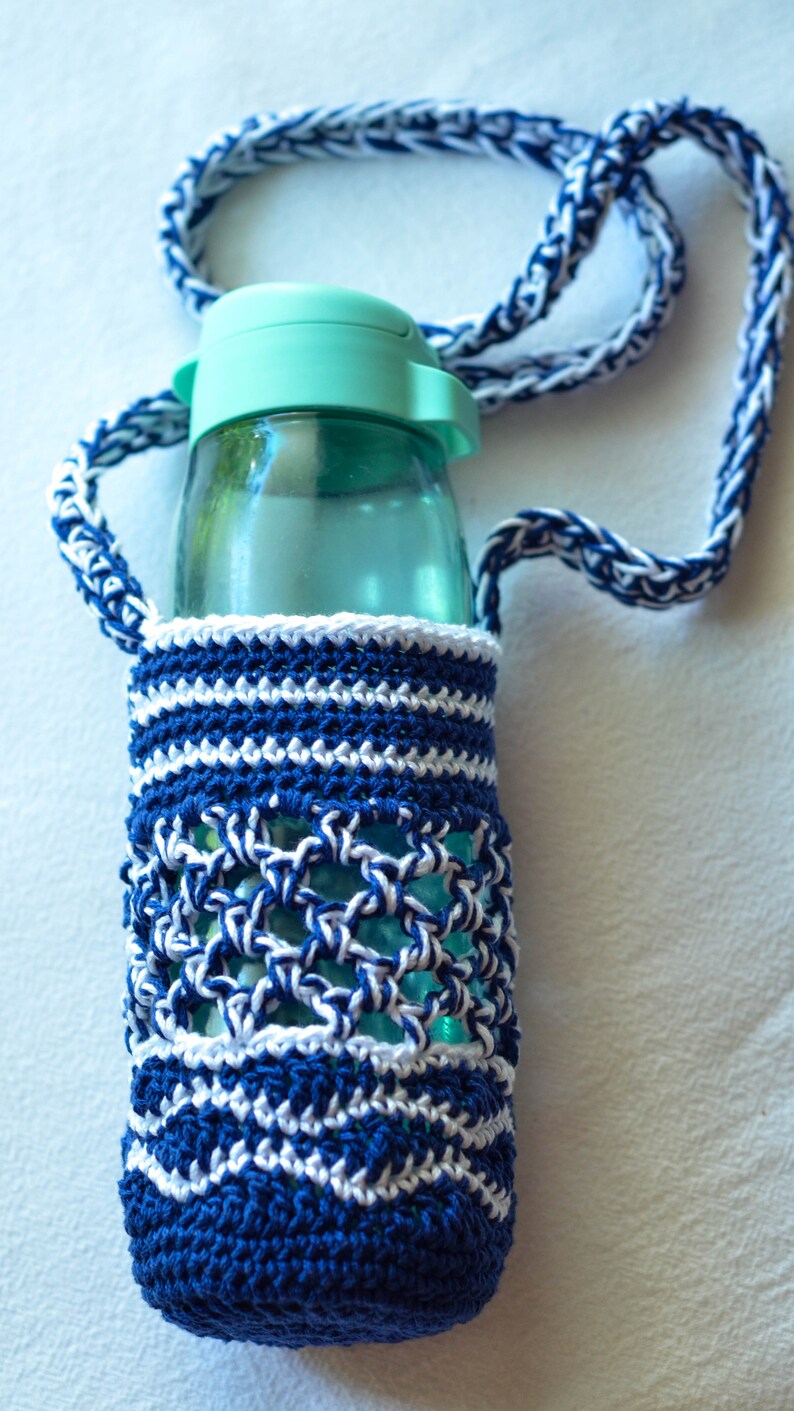 May include: A clear water bottle with a teal lid is encased in a handmade crochet holder. The holder is navy blue and white, with a matching strap. The crochet design features a mix of solid and openwork patterns.