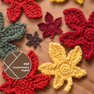 Op de afbeelding: Een verzameling handgemaakte gehaakte bladeren in herfstkleuren: rood, geel, groen en bruin. De bladeren zijn gerangschikt op een houten oppervlak. De afbeelding bevat een cirkelvormige afbeelding met de tekst "PDF Crochet Pattern English".