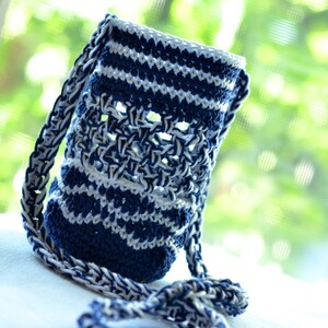 May include: A handmade, blue and white crochet water bottle holder with a long strap. The holder features a striped pattern and an open weave design. The strap is also crocheted in a matching blue and white pattern. The holder is designed to carry a water bottle.